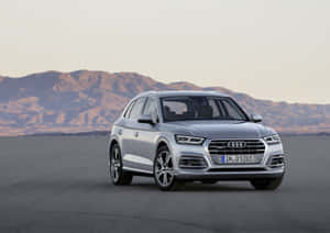 銀色 Audi Q5 SUV 停泊在沙漠中，背景有山脈。 — 奧迪 GIF 壁紙