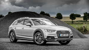銀色 Audi 旅行車停泊在碎石上，靠近石堆，天空多雲。 — 奧迪 GIF 壁紙