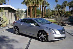 銀色 Cadillac ELR 停在有棕櫚樹和仙人掌的沙漠車道上。 — MacBook Air M2 壁紙