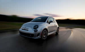 銀色Fiat 500在日落時分於濕滑道路上疾馳，帶有動態模糊效果。 — Steam Deck OLED 壁紙
