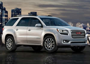 黃昏時濕潤屋頂上的銀色GMC Acadia SUV與城市天際線。 — 暮光 壁紙