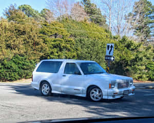 銀色GMC Typhoon SUV在綠樹灌木的道路上行駛。 — 5:4 壁紙
