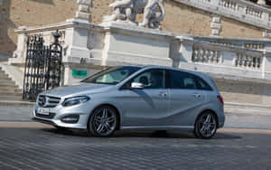 銀色 Mercedes-Benz B-Class 停在歷史石建築前，有獅子雕像和鐵門。 — Steam Deck 壁紙