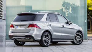 銀色 Mercedes-Benz GLE SUV 停泊在玻璃建築旁，窗戶有棕櫚樹倒影。 — 5120x2880 壁紙