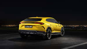 黃色林寶堅尼 Urus SUV 夜間停泊，俯瞰城市景觀。 — 蘭博基尼 壁紙