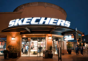 夜晚的Skechers零售店入口，帶有發光招牌和行人。