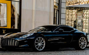 黑色Aston Martin跑車停泊在鵝卵石街道上，靠近奢侈品商店。 — Steam Deck 壁紙