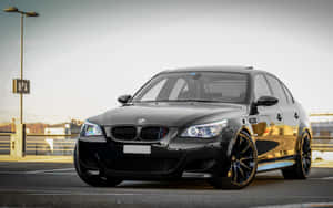 黑色BMW M5轎車停在瀝青上，配備定制輪圈和閃爍車頭燈。 — MacBook Air M1 壁紙