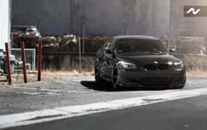 黑色BMW跑車停在工業圍欄附近的瀝青路上。 — Steam Deck OLED 壁紙
