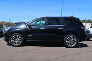 黑色GMC Acadia SUV停泊在陽光明媚的停車場，旁邊有其他汽車。 — Surface Pro 壁紙