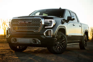 黑色GMC Sierra Denali皮卡車停在夕陽下的碎石路上。 — MacBook 壁紙