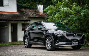 黑色Mazda CX-9 SUV停泊在一座有綠色樹木的風化房屋前。 — MacBook Pro 13 壁紙