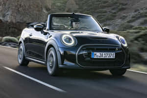 黑色MINI Cooper S Convertible在日落時分行駛在山路上。 — Surface Pro 壁紙