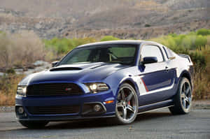 藍色福特野馬Shelby GT500停泊在山丘和灌木附近的碎石上。 — 日落 壁紙