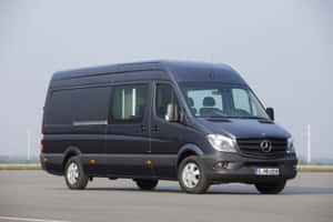 深灰色 Mercedes-Benz Sprinter 客貨車停泊在鋪砌場地上，背景有風力發電機。 — MacBook Air 15 壁紙