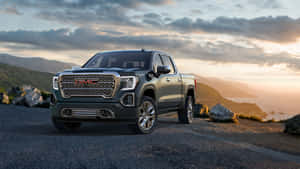 深綠色 GMC Sierra 皮卡車停在日落時分俯瞰海洋的懸崖上。 — iMac 壁紙