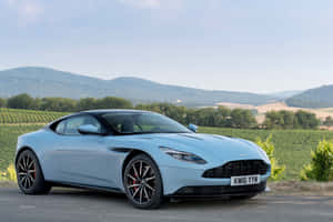 淺藍色Aston Martin跑車停泊在風景優美的道路上，背景有葡萄園和山脈。 — Surface Pro 壁紙