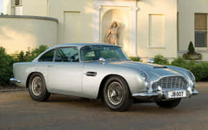 銀色經典Aston Martin DB5停泊在一棟帶有雕像的莊嚴奶油色大宅前。 — Steam Deck 壁紙