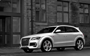 銀色Audi Q7 SUV停泊在城巿街道旁的石建築物旁邊。 — Steam Deck 壁紙