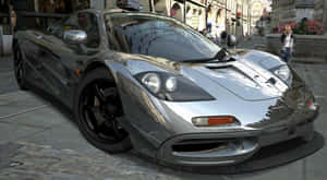 銀色McLaren F1超級跑車停放在歐洲城市街道上，周圍有歷史建築。 — 4K 法拉利 壁紙