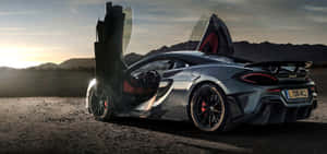 銀色McLaren跑車，鷗翼車門打開，停在日落時分的沙漠中。 — 超寬螢幕 壁紙