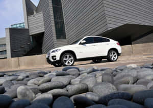 白色BMW X6 SUV停泊在現代建築物附近，前景有灰色石頭。 — 平治 C300 壁紙