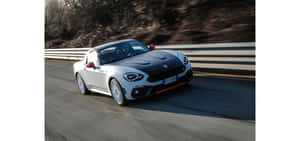白色Fiat 124 Spider在彎曲的道路上疾馳，帶有動態模糊。 — 超寬螢幕 壁紙