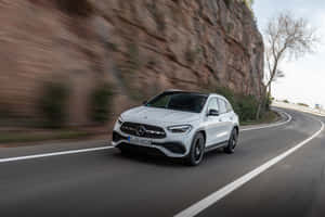 白色 Mercedes-Benz GLA 45 AMG 在蜿蜒的山路上快速行駛。 — Surface Laptop 壁紙