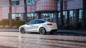 白色 Tesla Model 3 停泊在鵝卵石上，前面是現代建築，有棕櫚樹，日落時分。