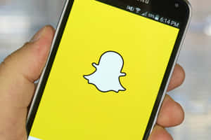 手拿智能手機，黃色屏幕上顯示Snapchat應用程式標誌。