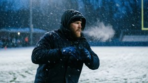 穿黑色冬季裝備的男人在冰凍田野的飄雪中呼出暖氣