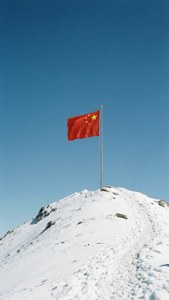 紅色中國國旗帶黃色星星在積雪山頂上飄揚，藍天背景