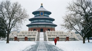一個穿著紅色外套的人，在冬雪中走向天壇。