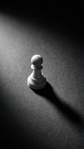白色國際象棋兵被聚光燈照亮在深色紋理表面上，帶有長影子