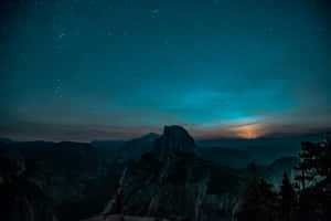 Half Dome 山脈輪廓在繁星點點的藍綠色夜空下，地平線閃耀著光芒