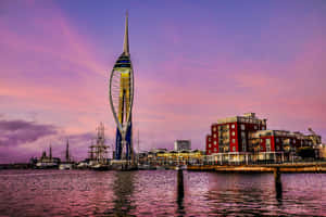 Spinnaker Tower 在日落時亮起，粉紅色和紫色的天空倒映在港灣水中。 — 日落大道 壁紙