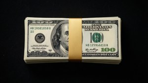 黑色背景上以金色帶子捆綁的百元美鈔堆