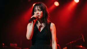 女歌手在紅色燈光下現場舞台表演，皮膚上有汗水。