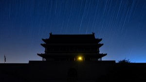 夜間星軌下古老門樓的剪影，有一扇發光的窗戶