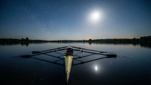 一艘黃色划艇在明亮的月亮和星空下平靜的水面上休息。