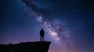 夜晚在銀河系下的懸崖邊緣站立的人