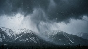 陰沉暴風雨天空下，積雪覆蓋的山脈，雪花飄落
