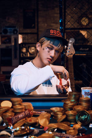 臉上帶有星星紋身的年輕男子，在昏暗的房間裡被糖果和結他包圍，手持硬幣。