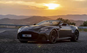 黑色Aston Martin開篷車停泊在碎石路上，金色日落。 — Steam Deck OLED 壁紙