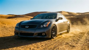 灰色 Infiniti 房車在日落時分於沙漠沙丘上疾馳。
