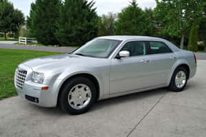 銀色Chrysler 300房車停在混凝土車道上，後面有綠化。 — Surface Pro 壁紙