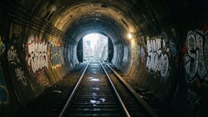 地鐵隧道，塗鴉牆壁和濕軌道通向明亮的城市出口。