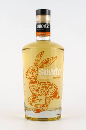 Suerte reposado龍舌蘭酒瓶，帶有橙色糖骷髏兔子插圖。