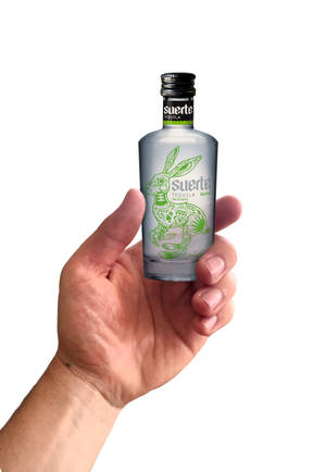 手拿著一個帶有綠色兔子插圖的Suerte Tequila Blanco酒瓶。