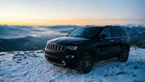 黑色Jeep Grand Cherokee停在白雪覆蓋的山上，俯瞰日出時霧氣瀰漫的山谷